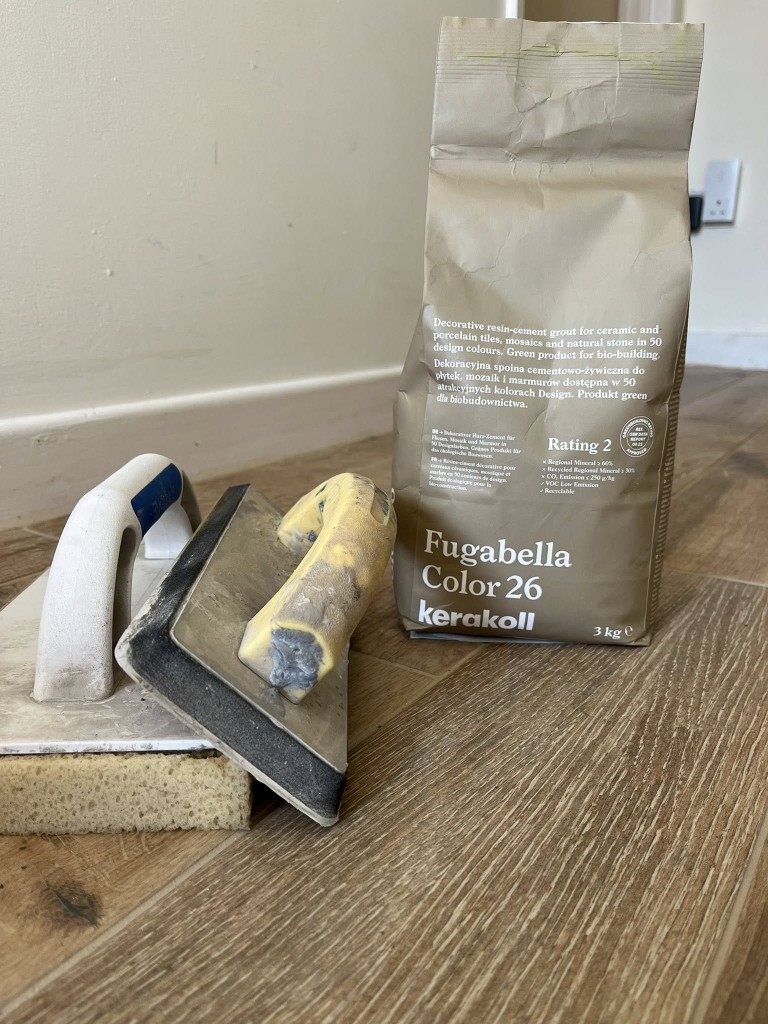 Grout float and sponge with a bag of Fugabella resin-cement grout on a wood-effect floor