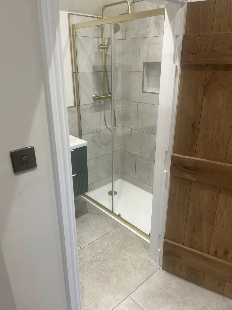 Brass-framed shower with marble-effect tiles seen through an oak doorway